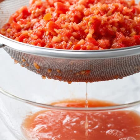 Pulse the tomatoes a couple of times in a food processor — enough to break them up but not purée them. Next, tip the mixture into a sieve set over a bowl and leave to drain away the excess liquid. This step matters more than it looks: tomato water in the Trapanese pesto makes the sauce thin and dull rather than textured and intense. Give it at least 5 minutes, or press gently if you're in a hurry.